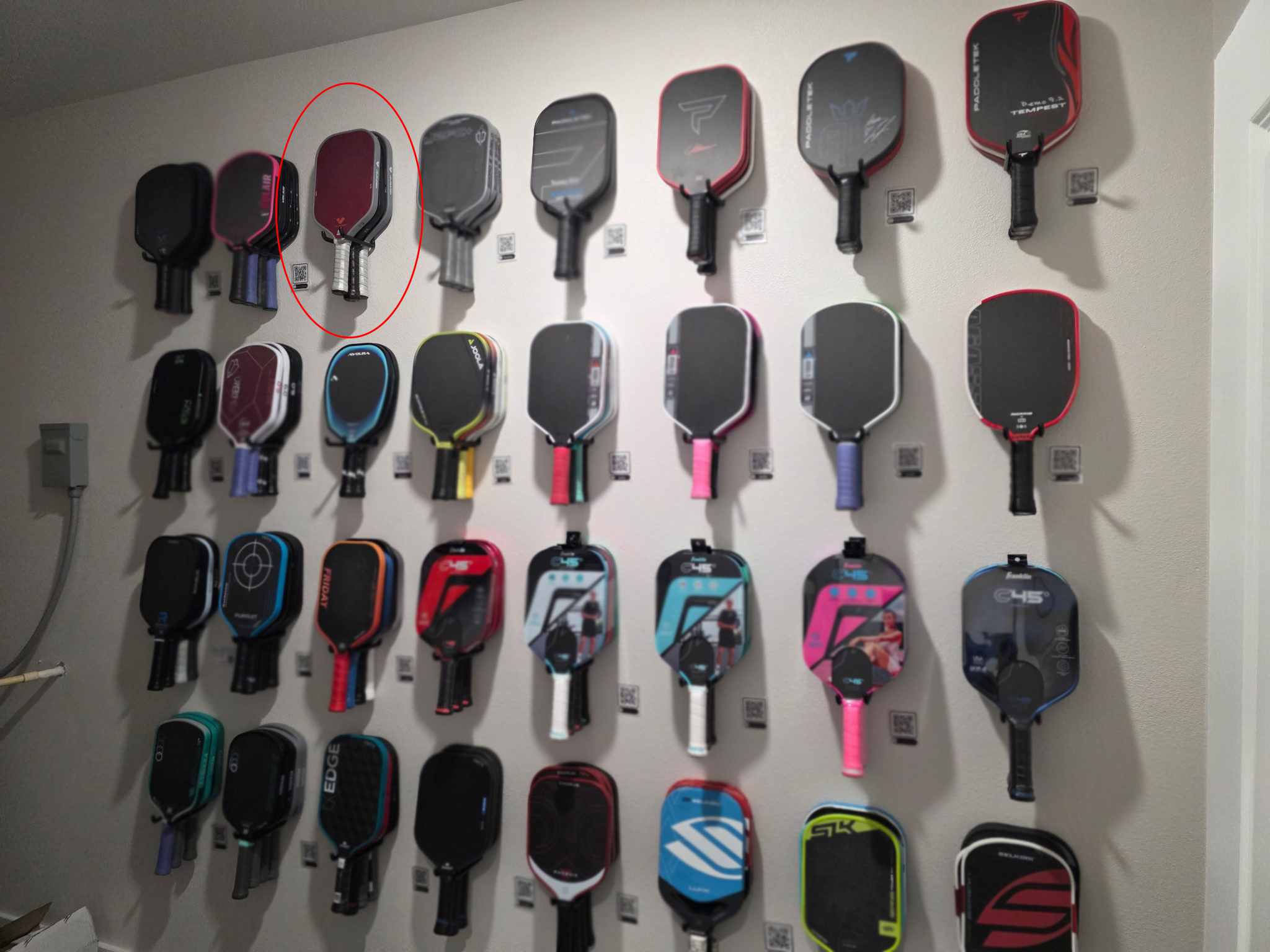 Wall display of various pickleball paddles with a red circle on one paddle.