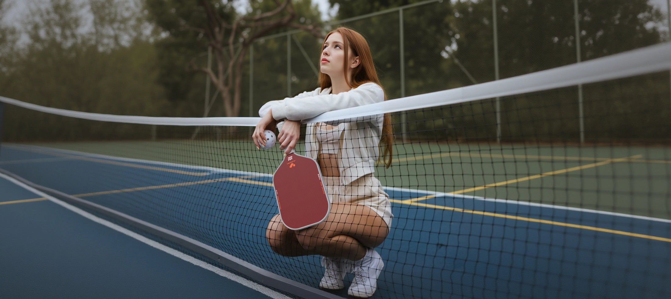 Woman on a pickleball court holding a jojolemon shark-002 pickleball paddle with a net in the foreground