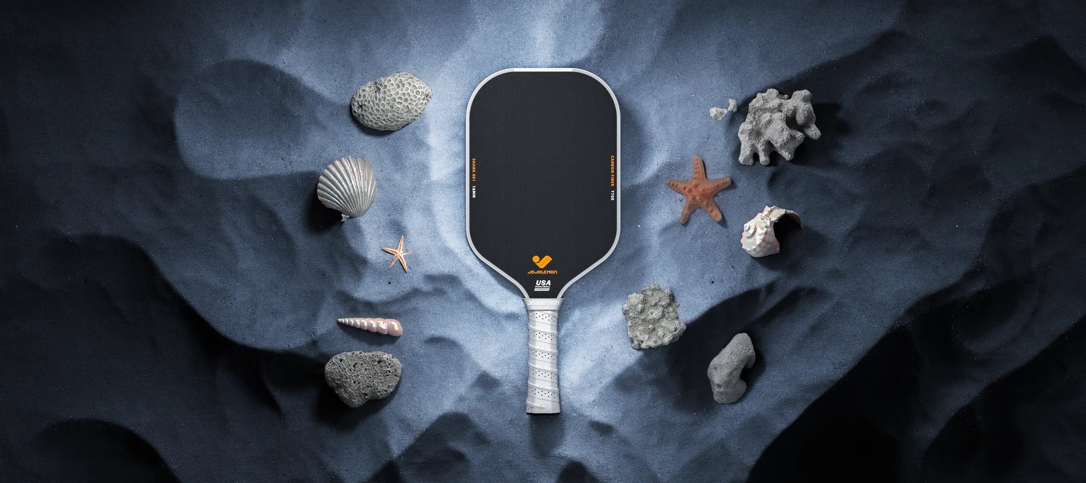 Pickleball paddle with gray handle on a textured blue background with starfish and coral.